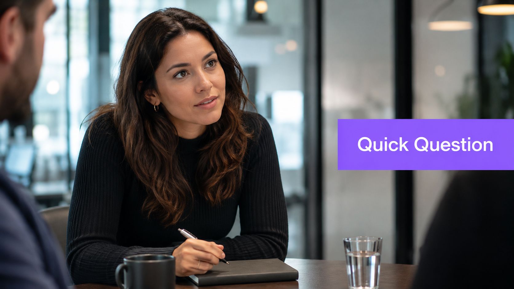 A professional woman participating in a business meeting, holding a pen while talking to colleagues.