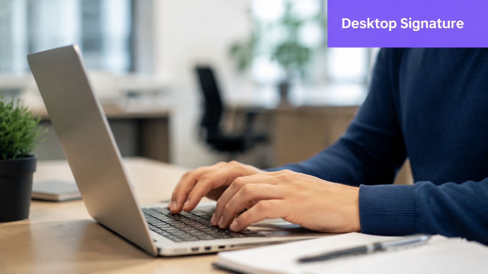 A person wearing a blue sweater typing on a silver laptop in an office environment.