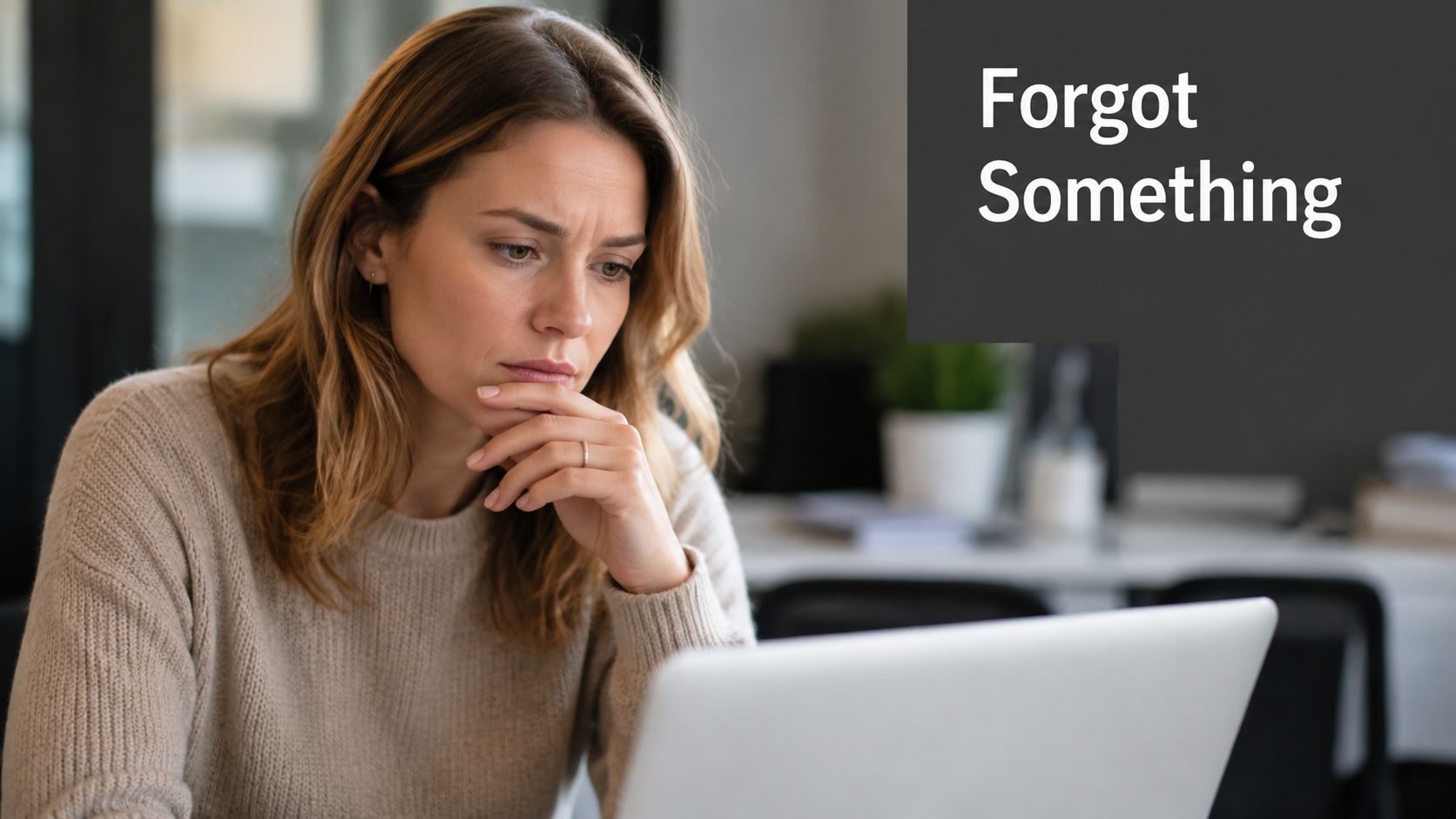 A concerned woman sitting at a desk looking at a laptop screen while thinking about something.